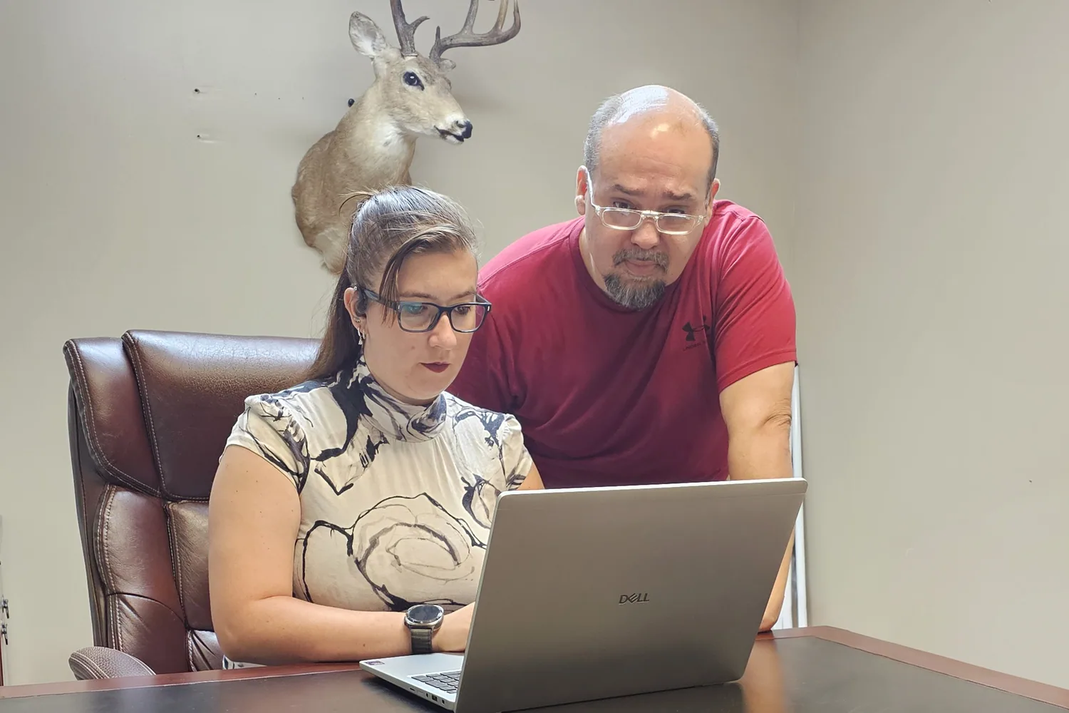 A woman typing on a laptop at a desk while a man leans in to look at the screen